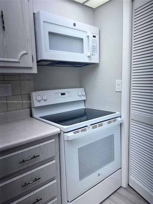 kitchen featuring white appliances, light wood-type flooring, and backsplash