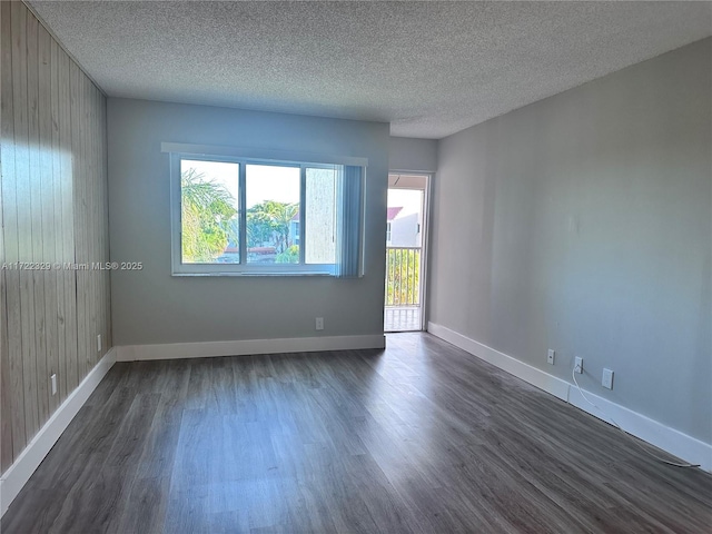 spare room featuring dark wood-type flooring, a textured ceiling, and wood walls