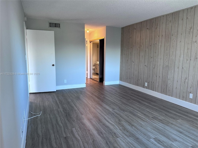 unfurnished room with dark hardwood / wood-style floors, a textured ceiling, and wooden walls