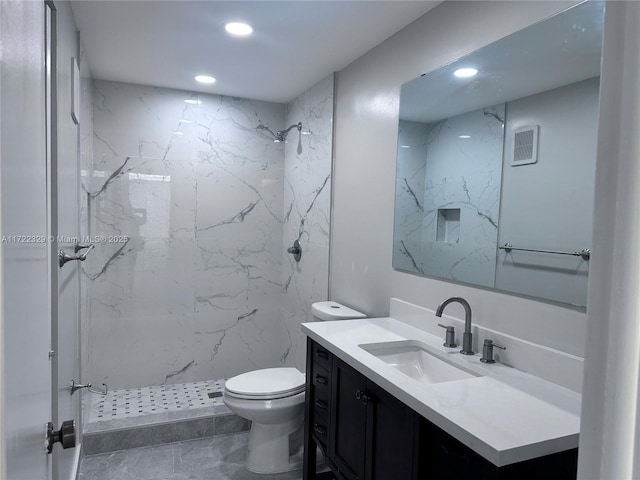 bathroom with vanity, tiled shower, and toilet