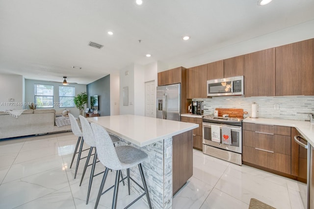 kitchen with a kitchen bar, appliances with stainless steel finishes, backsplash, ceiling fan, and a center island