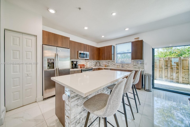 kitchen featuring decorative backsplash, a kitchen breakfast bar, stainless steel appliances, sink, and a kitchen island