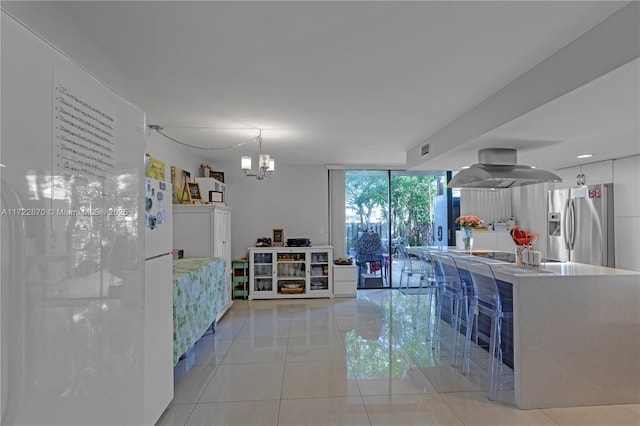 kitchen with an inviting chandelier, expansive windows, island exhaust hood, stainless steel fridge, and light tile patterned floors