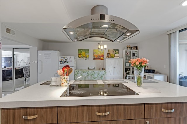 kitchen with black electric stovetop, white fridge, island range hood, and a kitchen island