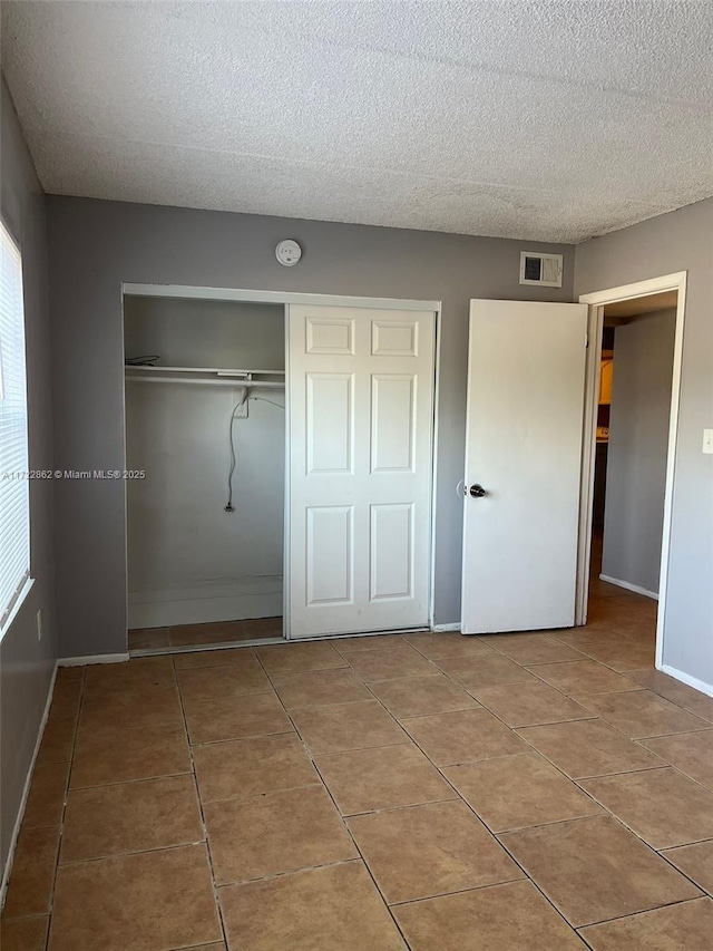 unfurnished bedroom with tile patterned flooring, a textured ceiling, and a closet