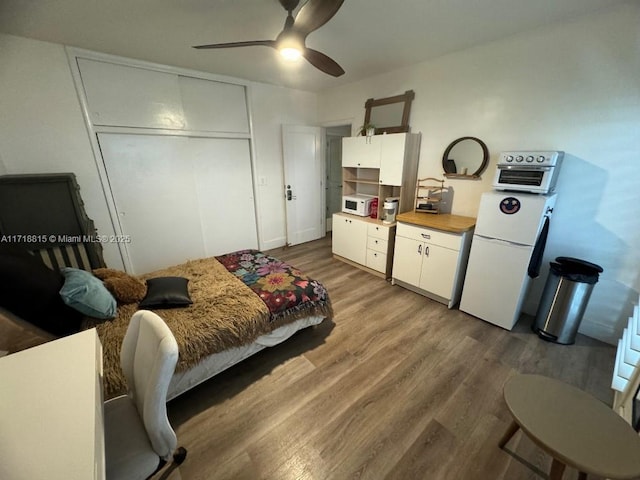 bedroom featuring fridge, dark hardwood / wood-style floors, ceiling fan, and a closet