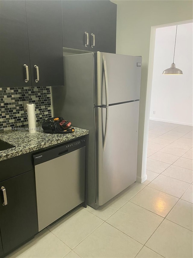 kitchen featuring stone countertops, backsplash, light tile patterned floors, appliances with stainless steel finishes, and decorative light fixtures