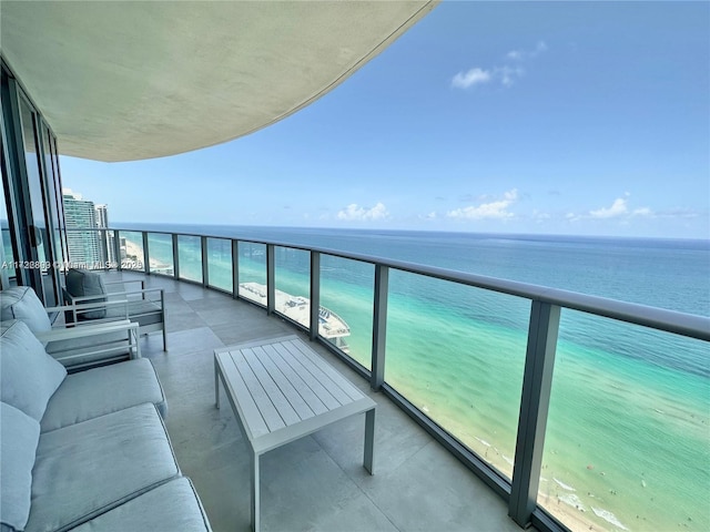 balcony with an outdoor living space, a water view, and a beach view