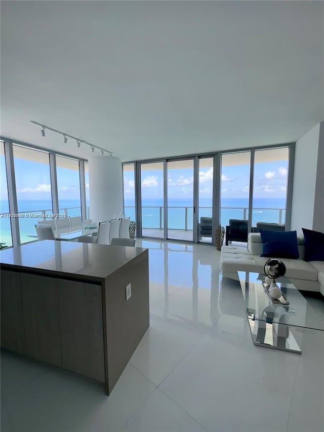 kitchen featuring rail lighting, floor to ceiling windows, light tile patterned floors, a water view, and a large island