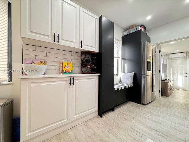 kitchen featuring light wood finished floors, stainless steel fridge, white cabinets, light countertops, and an AC wall unit