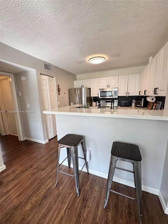 kitchen featuring white cabinetry, appliances with stainless steel finishes, tasteful backsplash, a kitchen breakfast bar, and dark wood-type flooring