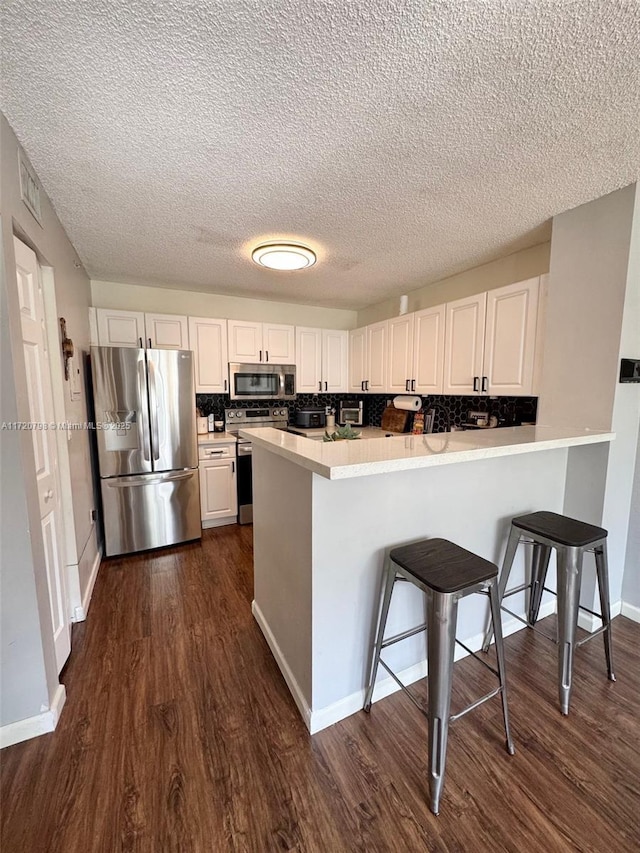 kitchen featuring kitchen peninsula, white cabinetry, stainless steel appliances, and a kitchen breakfast bar