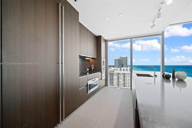 kitchen featuring sink, light tile patterned floors, expansive windows, and a water view