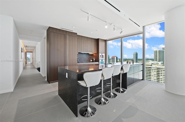 kitchen with a breakfast bar, floor to ceiling windows, decorative backsplash, dark brown cabinetry, and a center island