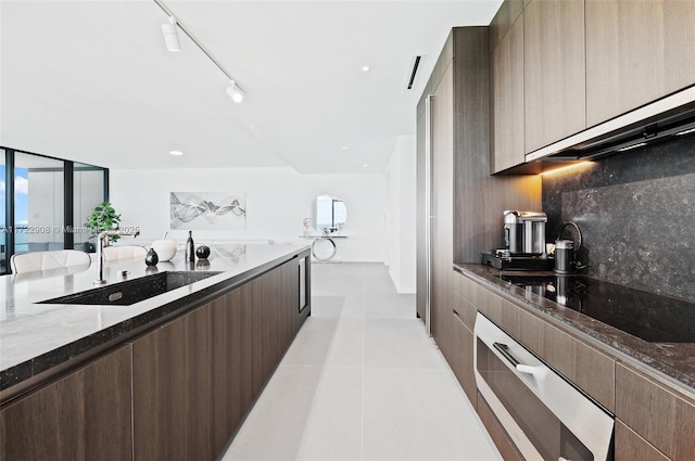 kitchen with dark stone countertops, black electric stovetop, oven, sink, and track lighting