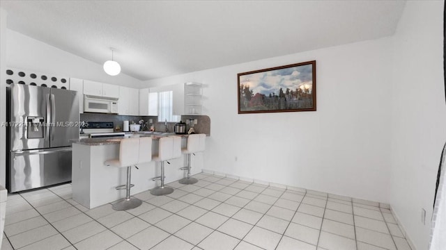 kitchen featuring kitchen peninsula, appliances with stainless steel finishes, a kitchen breakfast bar, vaulted ceiling, and white cabinetry