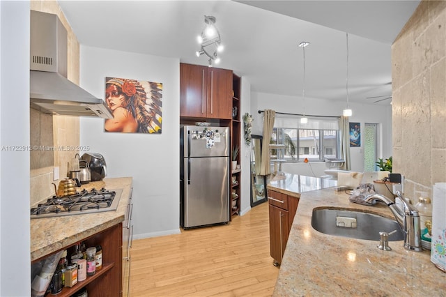 kitchen featuring sink, wall chimney exhaust hood, stainless steel appliances, light stone counters, and light hardwood / wood-style flooring