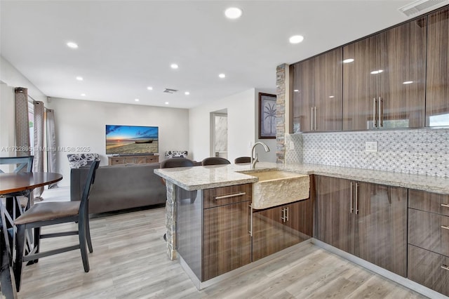 kitchen featuring kitchen peninsula, light hardwood / wood-style flooring, light stone countertops, and sink