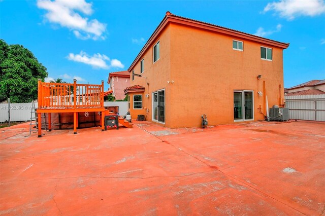 back of house with a wooden deck, a patio area, and a lawn