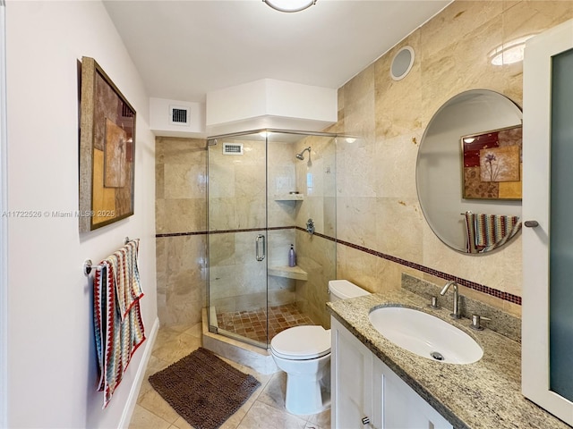 bathroom featuring tile patterned floors, an enclosed shower, toilet, vanity, and tile walls