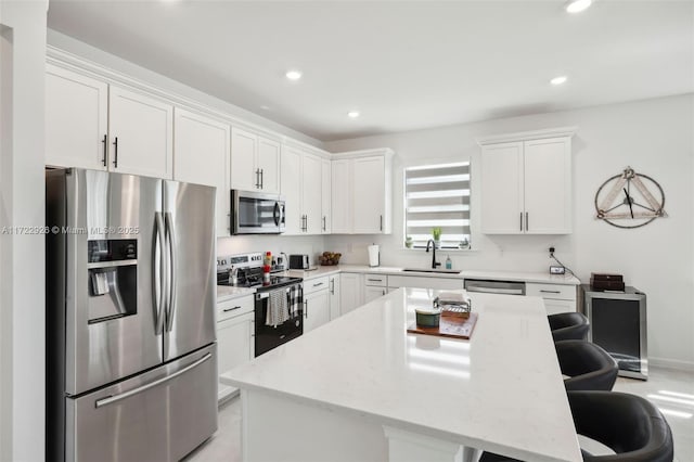 kitchen featuring white cabinets, a kitchen bar, appliances with stainless steel finishes, a sink, and a center island