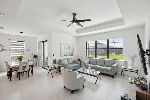 living room featuring a raised ceiling, ceiling fan, crown molding, and light tile patterned floors