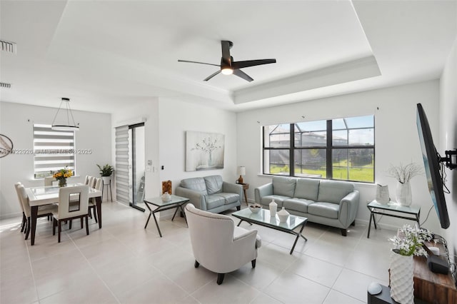 living room featuring light tile patterned flooring, a tray ceiling, visible vents, and a ceiling fan