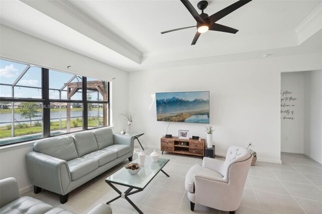 living area featuring a raised ceiling, light tile patterned floors, baseboards, ceiling fan, and ornamental molding