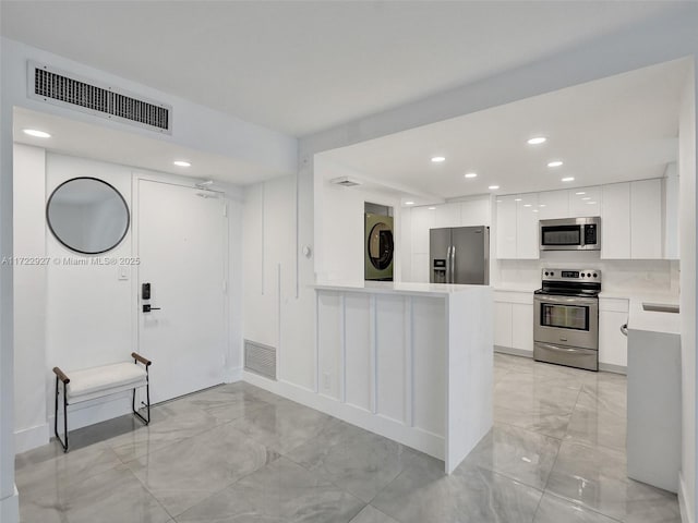 kitchen featuring stacked washer / dryer, white cabinetry, kitchen peninsula, and stainless steel appliances