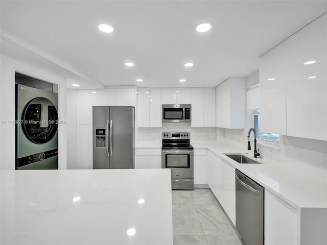 kitchen featuring sink, stacked washer and dryer, tasteful backsplash, white cabinetry, and stainless steel appliances