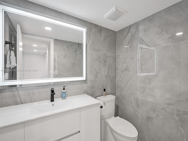 bathroom with vanity, toilet, and tile walls