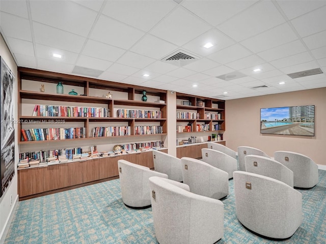 interior space featuring carpet flooring, built in shelves, and a drop ceiling