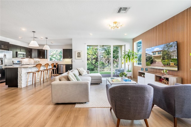 living room with a chandelier, a healthy amount of sunlight, light hardwood / wood-style floors, and wooden walls