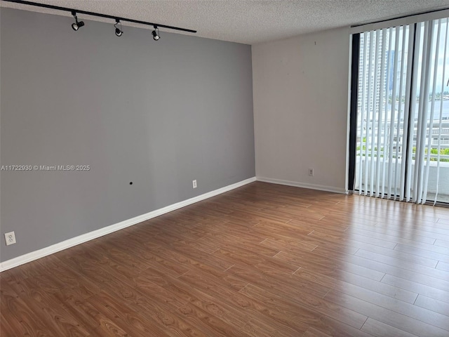 spare room with a wealth of natural light, rail lighting, a textured ceiling, and a wall of windows