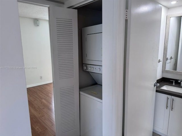 clothes washing area with stacked washer and dryer, hardwood / wood-style flooring, and sink