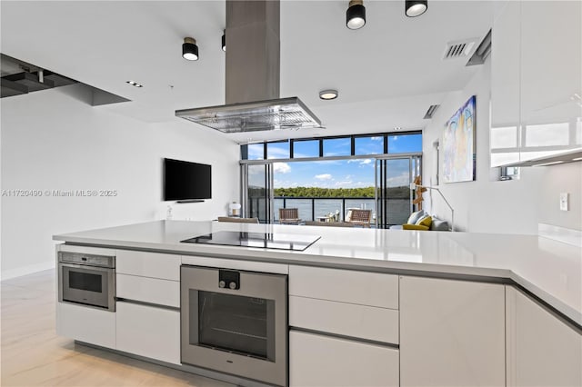 kitchen with white cabinets, stainless steel oven, black electric stovetop, and island exhaust hood