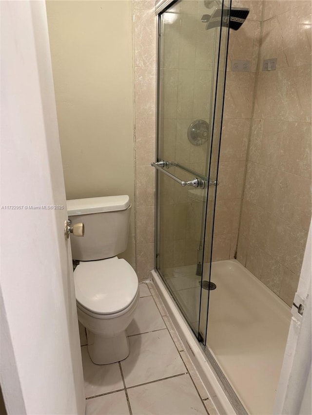 bathroom featuring tile patterned flooring, toilet, and a shower with door