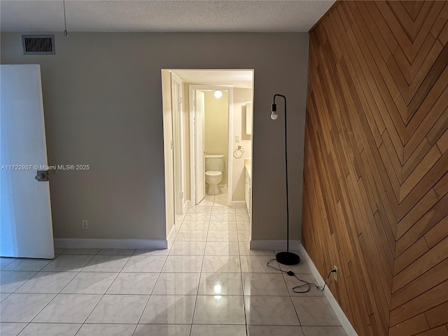 hall with light tile patterned floors, a textured ceiling, and wooden walls