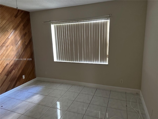 unfurnished room with wood walls, light tile patterned floors, a textured ceiling, and a wealth of natural light