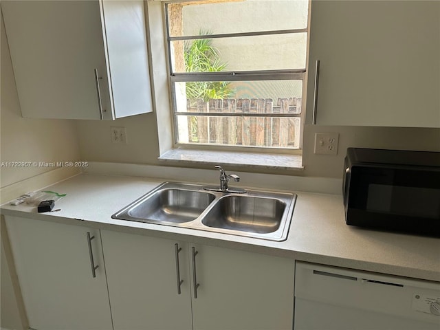 kitchen with white dishwasher, white cabinetry, a healthy amount of sunlight, and sink