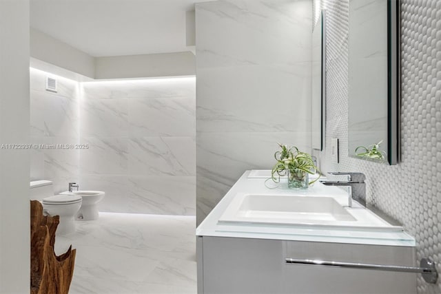 bathroom with vanity, toilet, a bidet, and tile walls