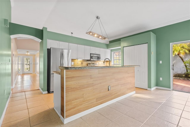 kitchen with arched walkways, light tile patterned flooring, stainless steel appliances, white cabinets, and decorative backsplash