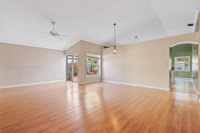 unfurnished living room featuring arched walkways, light wood-style flooring, a ceiling fan, baseboards, and crown molding