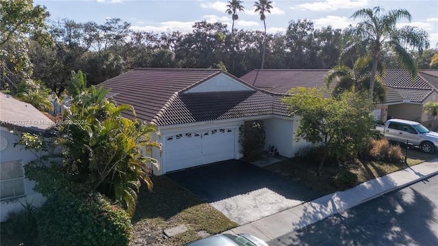 ranch-style house featuring a tiled roof, aphalt driveway, an attached garage, and stucco siding