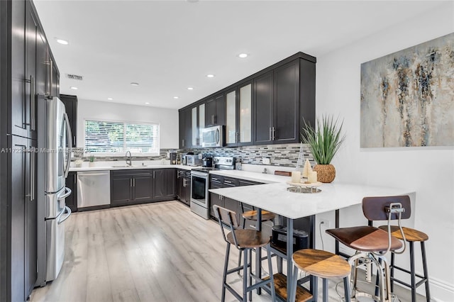 kitchen with a kitchen breakfast bar, light hardwood / wood-style flooring, tasteful backsplash, kitchen peninsula, and stainless steel appliances