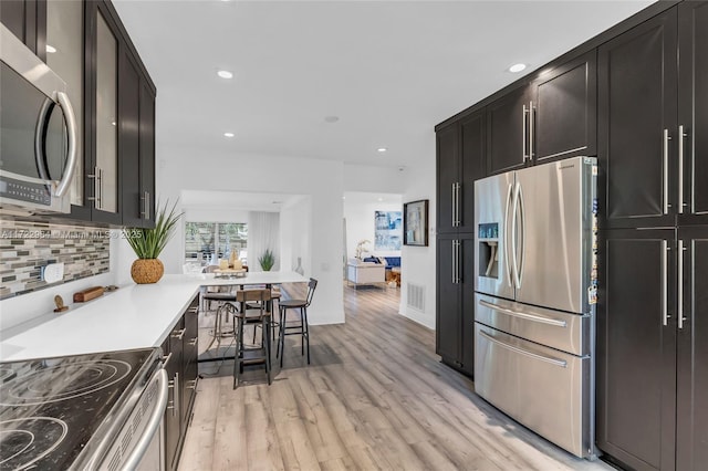 kitchen featuring decorative backsplash, light wood-type flooring, stainless steel appliances, and a breakfast bar