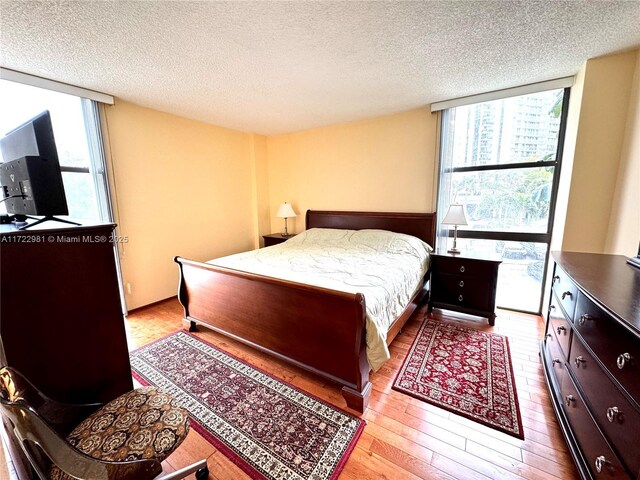 bedroom with a textured ceiling, light hardwood / wood-style flooring, and expansive windows