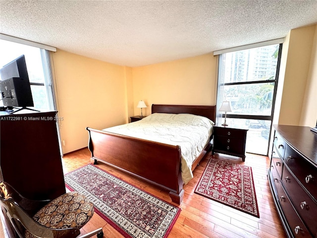 bedroom with wood-type flooring, floor to ceiling windows, and a textured ceiling