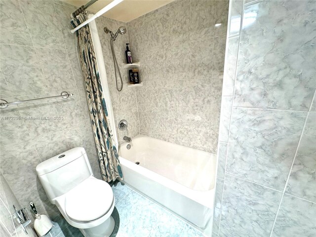 bathroom featuring toilet, shower / bath combo with shower curtain, and tile walls