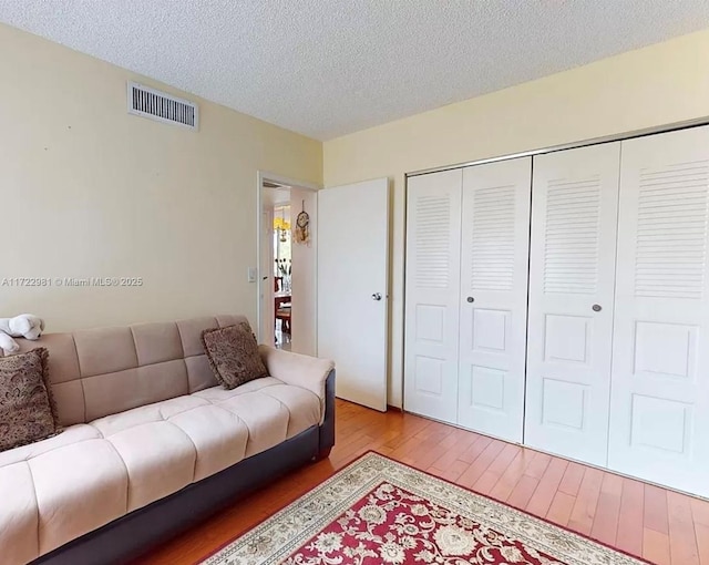 living room featuring a textured ceiling, visible vents, and wood finished floors